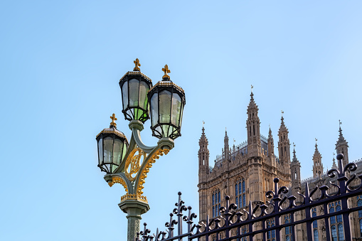 Decorative street light and wrought iron railings outside of the Houses of Parliament, London, UK. Blue sky background with space for text.