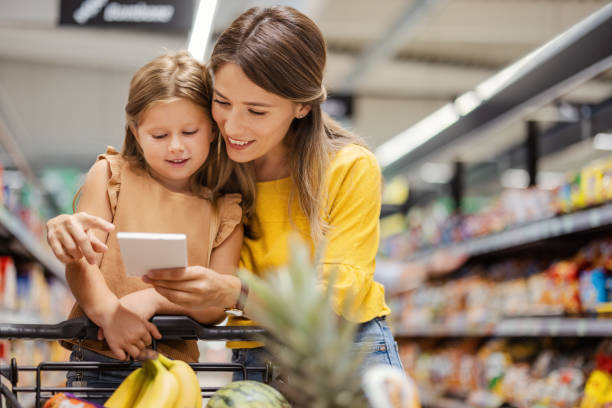 Mother and Child Looking at Grocery List in the Supermarket Mother and child looking into grocery list at grocery store shopping list stock pictures, royalty-free photos & images