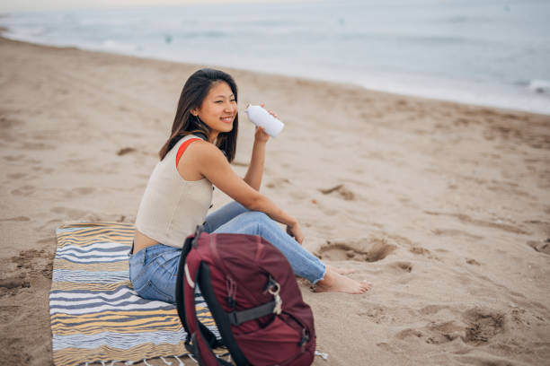 istock Young chinese woman siting on a beach drinking from bottle 1425143463