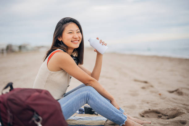 istock Young chinese woman siting on a beach drinking from bottle 1425143512