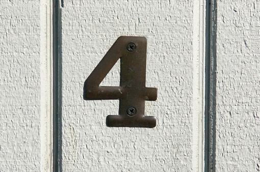 House address number four in metal against white wood panels