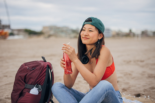 Young Chinese woman sitting on a beach and drinking soda