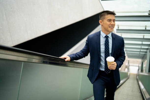 istock A businessman holding a coffee cup travelling up an escalator 1425145278