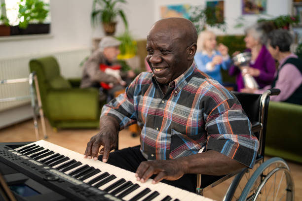 Adult Day Services Center musical activities Using music for an uplifting therapy for the members of a local community center, a cheerful man is playing a keyboard at the front common room stock pictures, royalty-free photos & images