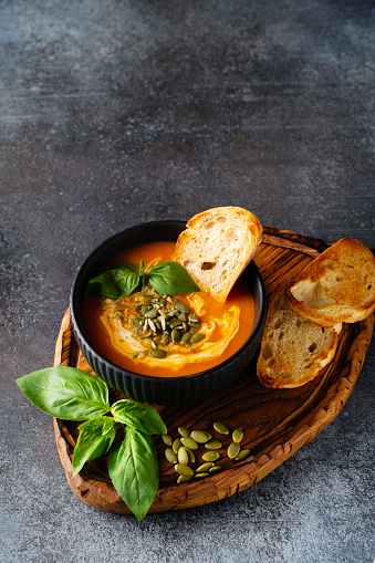 Pumpkin soup with bread, seeds and basil leaf on dark background, top view, copy space, vertical