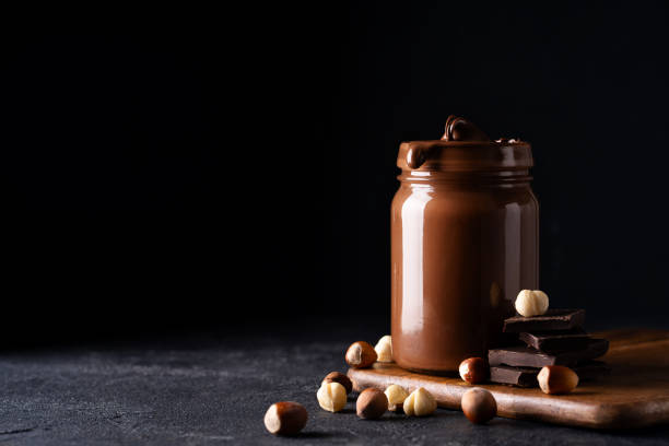 istock Chocolate paste in jar with nuts on cut wooden board 1425146094
