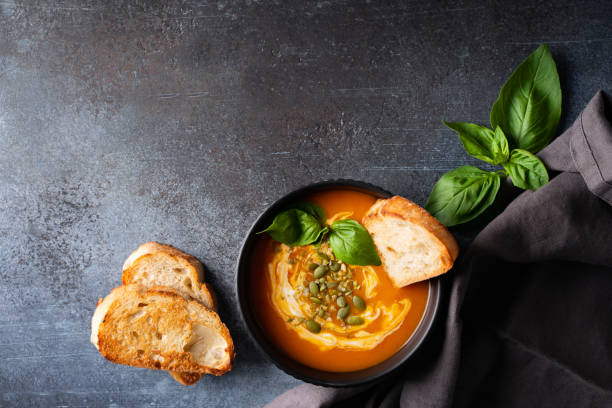 istock Pumpkin soup with bread, seeds and basil leaf on dark background 1425146116