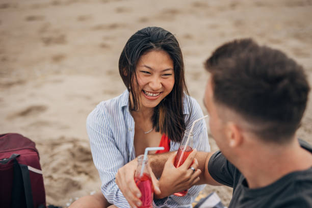 istock Young multi ethnic couple sitting on a beach drinking soda 1425147792