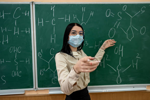 istock young female teacher in protective mask standing near blackboard 1425149889
