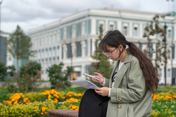 istock A girl sits on a bench on the street with documents in her hands and using her phone 1425150564