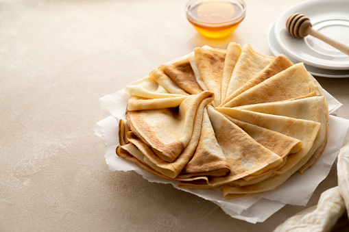 Pancakes or thin crepes with honey on neutral, warm background. Delicious homemade food.