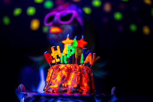 A girl is holding a birthday cake under neon lights