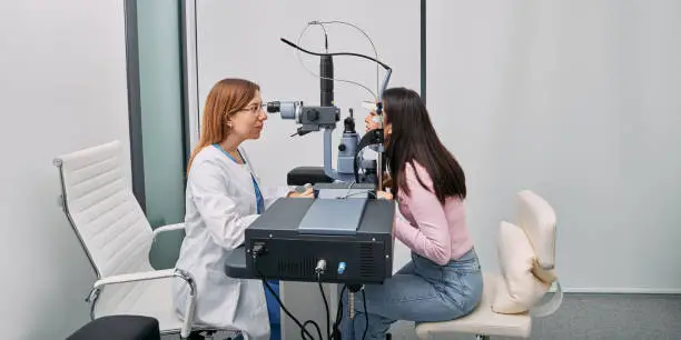 Asian woman getting eye exam at ophthalmology clinic with optometrist. Ophthalmology. Side view