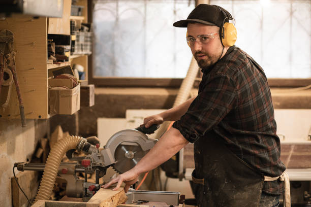 istock Carpenter worker in protective apron and headphones use grinder machine, cutting wood planks with circular, rotate saw 1425153020