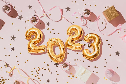 Gold 2022 balloons on a pink background with confetti and Christmas shiny balls, flat lay. New Years celebration concept