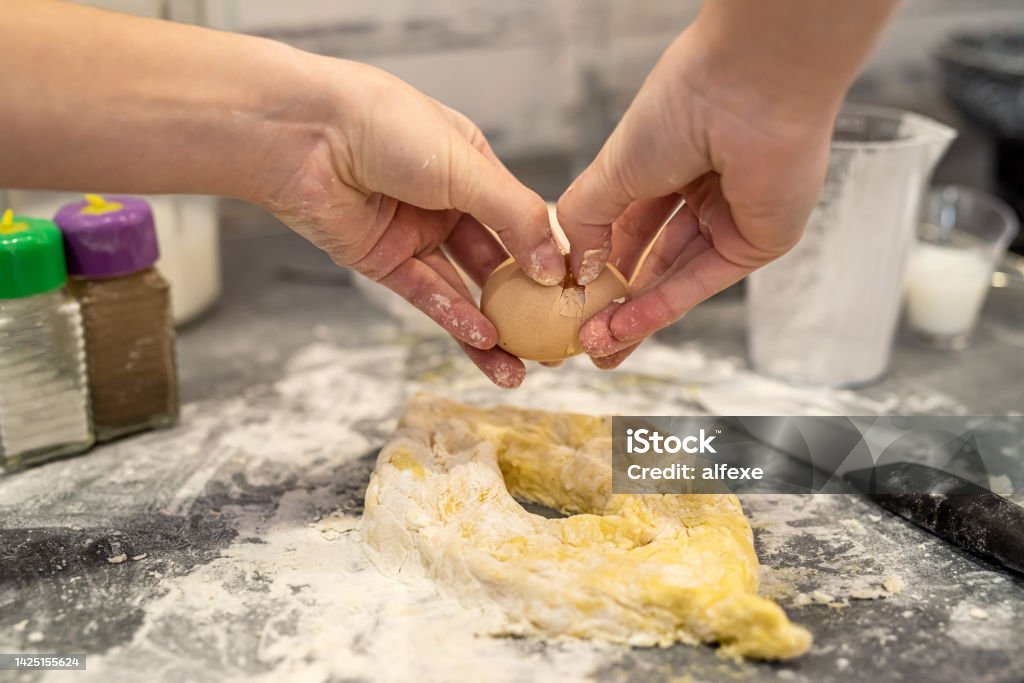 woman is fighting in the kitchen breaking eggs into flour and kneading dough into dumplings. young beautiful woman is fighting in the kitchen breaking eggs into flour and kneading dough into dumplings. The concept of cooking in the kitchen Adult Stock Photo