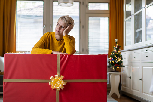 A middle aged woman is looking sad when receiving a huge Christmas gift