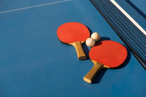 Photo of Table tennis ping pong paddles and white ball on blue board.