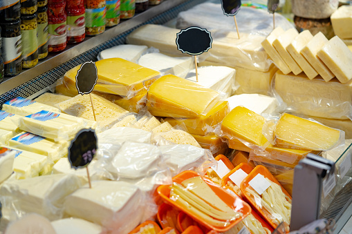 Fresh cheese on display at illuminated counter. Close-up of healthy dairy products. Interior of convenience store.