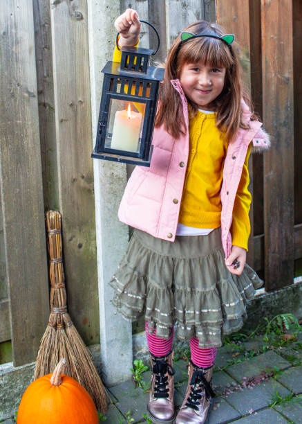 jolie fille mignonne de 9 ans debout avec une lanterne dans la cour sur le fond d’une clôture en bois brut. joyeux concept de vacances d’halloween. - 6 7 years little girls child standing photos et images de collection