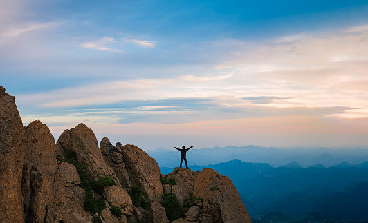 Positive Man standing on top of the mountain with arms raised celebrating his success