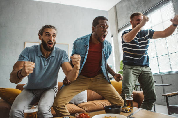 Watching soccer championship at home Diverse group of men watching soccer match at home and cheering for favorite team. excited football fan cheering for his team on tv stock pictures, royalty-free photos & images