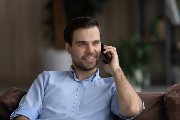 Happy millennial man holding cellphone conversation at home.