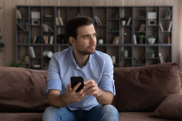 istock Dreamy happy young handsome man holding cellphone in hands. 1425167352