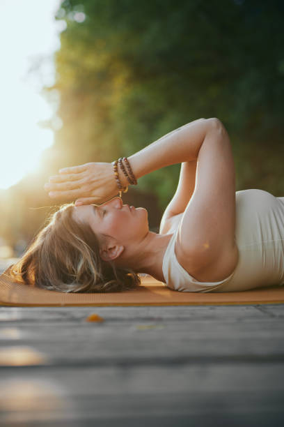 istock A mindful woman is lying on her back and holding hands in a namaste position while practicing breathing on the dock near the river in nature. 1425168461
