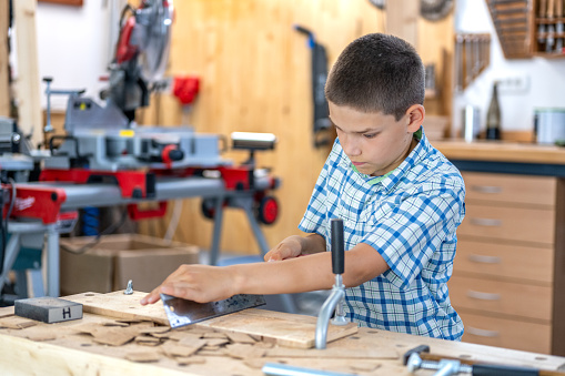 Boy with saw cutting wooden plank in workshop.