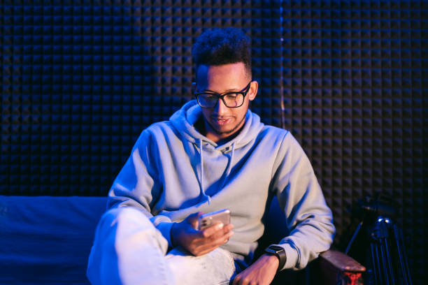 istock Curly man wearing glasses hold smartphone while sitting on couch 1425171704