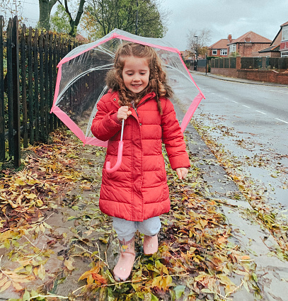 A happy little girl is walking through leaves in the autumn.