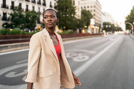 Stylish young adult woman with short hair looking away while crossing the street in the city