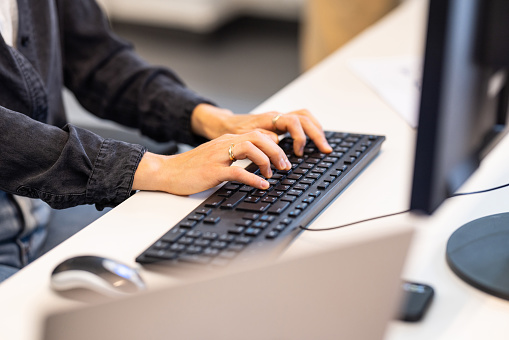 Close-up of businesswoman's hands using computer keyboard. Female professional is typing at desk in office