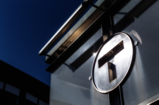 Cambridge, Massachusetts, USA - September 15, 2022: Close-up of silver metal letter T logo of the Massachusetts Bay Transportation Authority (MBTA) atop a station entrance. Low light, soft focus.