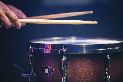 Drummer playing drum sticks on a snare drum on black background close up.