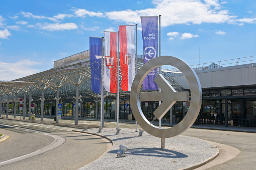 Linz, Austria - June 11, 2022: Exterior shot of the regional airport in Linz an der Donau (IATA: LNZ). The picture shows the flags with the circle of stars of the EU, the coat of arms of the city of Linz and the state of Upper Austria, as well as the logo of Linz Airport.