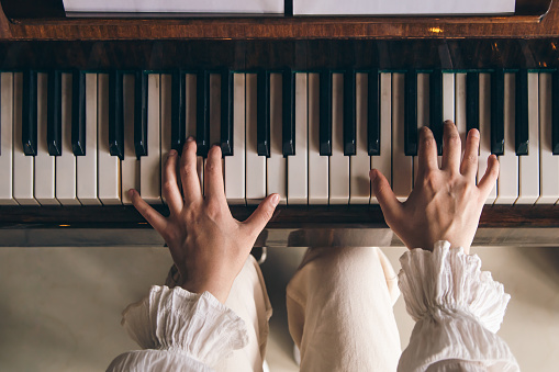 Female hands play on an old wooden piano, close-up, top view.