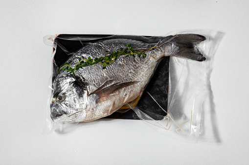 Raw stuffed dorado with rosemary in vacuum packing on a white background