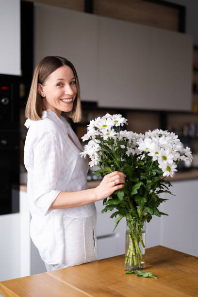 Beautiful woman putting fresh white flowers into a vase stock photo