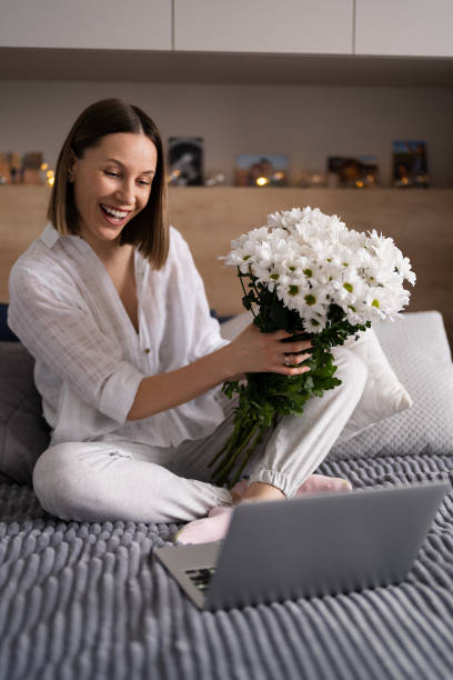 istock Woman communicating using a laptop while stating on bet with a bunch of white flowers 1425188948