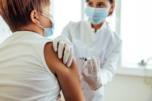 Professional nurse in a medical face mask giving a flu shot to her little patient