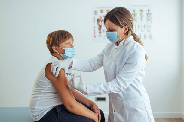 istock Female nurse in uniform and protective workwear making injection to young boy 1425191030
