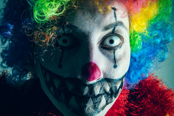 closeup of a scary evil clown wearing a dirty and ragged costume with a blank black space on the right