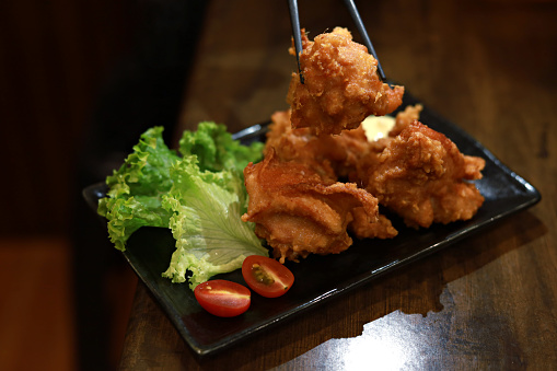 Close up chopsticks holding a Karaage or Japanese fried chicken serve with mayo on wooden table in Japanese restaurant.