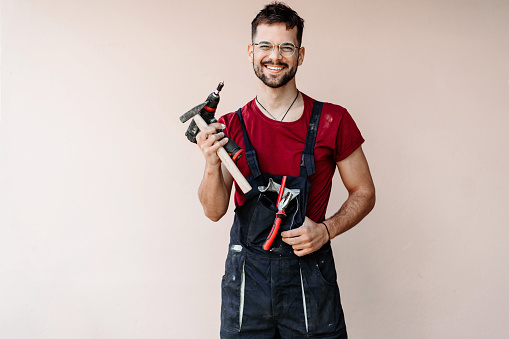 Portrait of a carpenter smiling and holding tools in front of a wall.