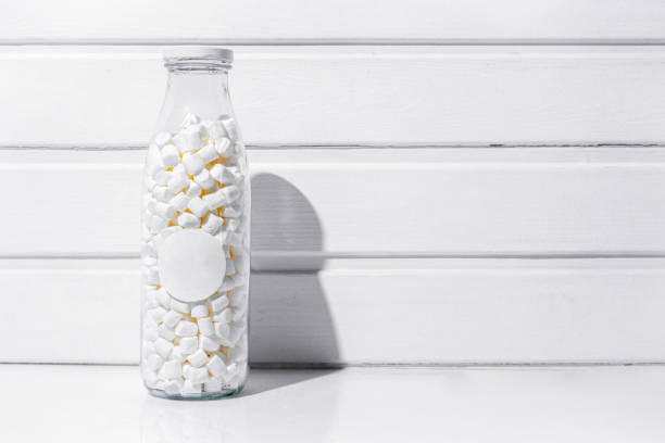 Transparent jar with marshmallows inside on white table and white wooden background
