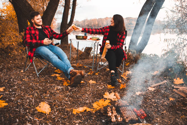 smiling happy couple resting near fire cooking food stock photo
