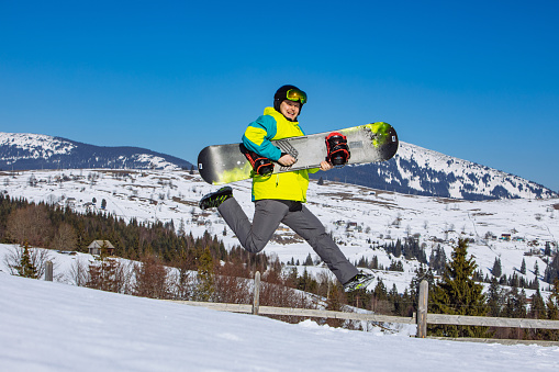 man jumping with snowboard in hands mountains on background. sunny day. having fun