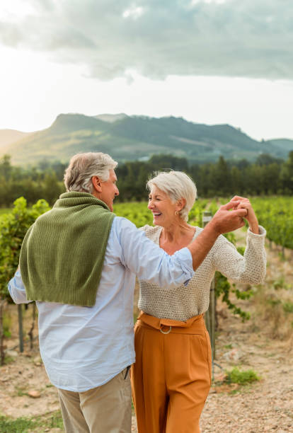 Happy elderly couple dancing at vineyard or wine farm, cheerful and positive energy. Active husband and wife having fun and bonding in nature. Senior man and woman enjoy relationship on outdoor date stock photo